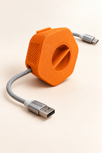 Enrouleur de câble portable Enroulo orange avec câble tressé USB-A vers USB-C, sur fond crème